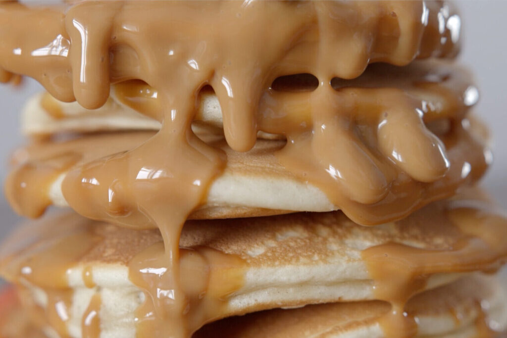 Imagen de la mantequilla de cacahuete/maní de Nitka Fitness. La fotografía muestra unos deliciosos pancakes saludables apilados, con la mantequilla de cacahuete/maní cayendo por encima.