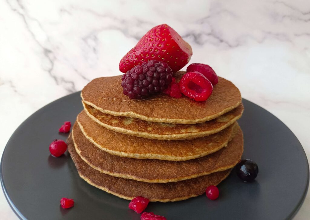 Imagen: Fotografía de la receta de pancakes saludables con plátano y avena de Nitka fitness. La fotografía muestea los pancakes apilados uno encima de otro, con frutos rojos por encima.