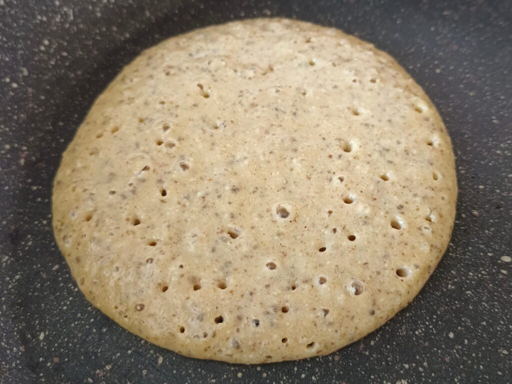 Foto del proceso de preparación de la receta de pancakes saludables con plátano y avena de Nitka fitness. La foto muestra el momento en el que podemos girar el pancake.