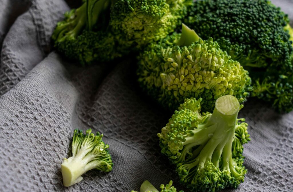 Imagen de brócoli crudo, recién cortado y dispuesto sobre un trapo de cocina gris, listo para ser condimentado y luego horneado. Una opción saludable y deliciosa para disfrutar de este nutritivo vegetal. Broccoli al horno de NitkaFitness.